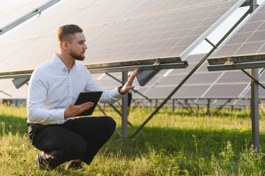 Dijital tabletli genç mühendis güneş çiftliğindeki fotovoltaik panelleri denetliyor, yenilenebilir enerji üretimi ve verimliliğini izliyor.