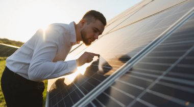 Güneş panelini inceleyen adam temiz enerji, sürdürülebilirlik ve yeşil teknolojiyi güneş çiftliğinde sergiliyor.