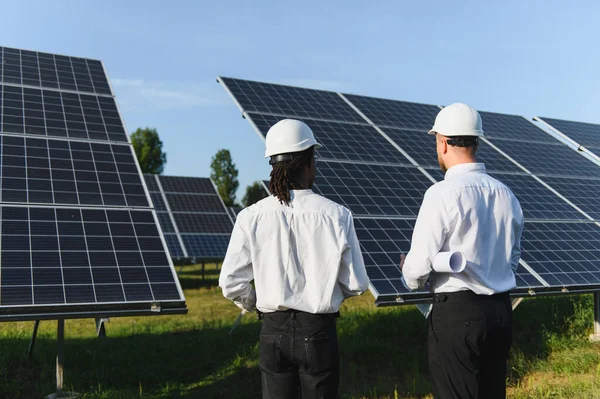 Bir enerji santralinde güneş paneli kurulumunu değerlendirip sürdürülebilir enerjiye odaklanan iki mühendis.