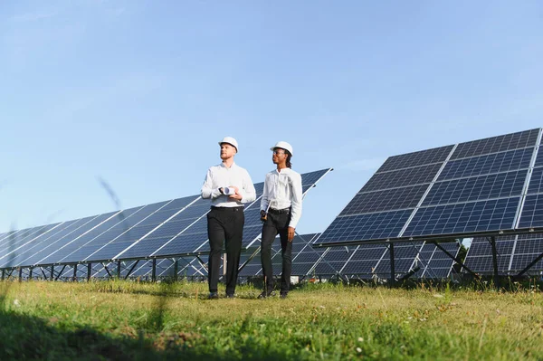 Temiz enerji ve sürdürülebilirliğe odaklanmış, yürüyen ve büyük bir güneş enerjisi santralini izleyen iki farklı mühendis.