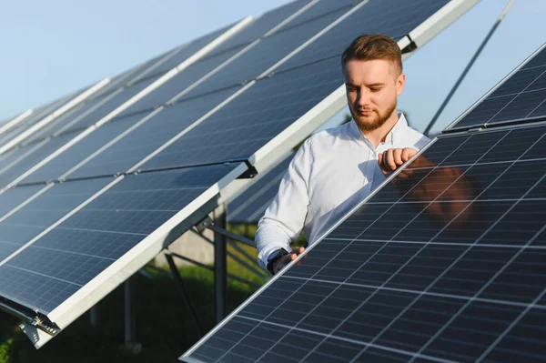 Beyaz gömlekli bir adam fotovoltaik çiftlikte güneş panellerini kontrol ediyor, sürdürülebilir temiz enerjiyi ve gelecekteki gücü simgeliyor.