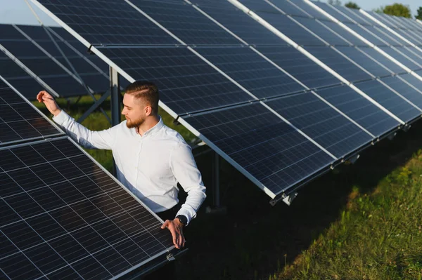 Bir güneş çiftliğindeki güneş panellerini denetleyen genç erkek mühendis, temiz, verimli yenilenebilir enerji gelişimi performansını izliyor