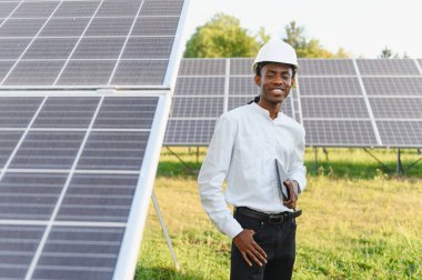 Güneş panellerinin yanında dururken gülümseyen Afrikalı Amerikalı mühendis yenilenebilir enerji ve sürdürülebilir kaynakları temsil ediyor.