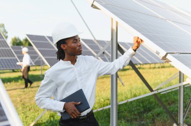 Siyah şapkalı Afro-Amerikan adam güneş panelini denetliyor, elinde tablet var. Temiz enerji ve sürdürülebilirliği teşvik etmek