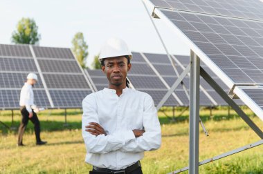 Başlık takan mühendis, güneş paneli alanında çapraz kollarıyla durarak yenilenebilir enerji ve sürdürülebilirliğe odaklanıyor.