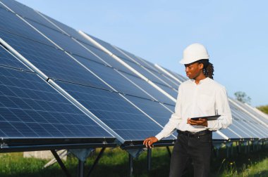Başlık takan ve elinde dijital tablet bulunan genç adam, sürdürülebilir enerji üreten fotovoltaik panelleri kontrol ediyor.