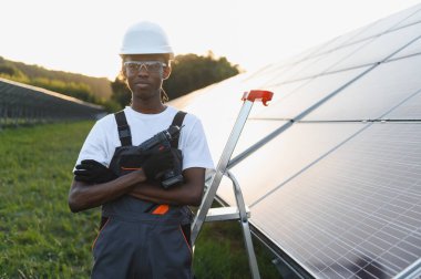 Güneş enerjisi çiftliğinde elinde matkap tutan ve sürdürülebilir enerji gelişimine katkıda bulunan erkek teknisyen.