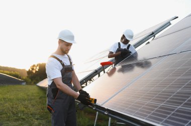 Güneş panelleri üzerinde çalışan kasklı ve tulumlu işçiler, yenilenebilir enerji sistemini temiz enerjiyi kullanmak için bağlıyorlar.