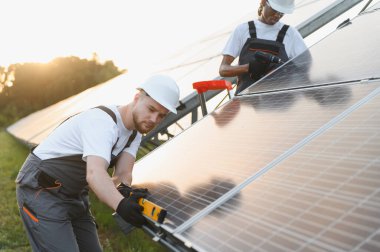 Güneş panelleri üzerinde çalışan iki teknisyen, temiz ve sürdürülebilir elektrik için yeni bir güneş enerjisi dizisi kuruyor.