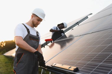 Çeşitli işçiler bir alana fotovoltaik güneş panelleri kurarak temiz ve sürdürülebilir enerji için elektrik üretiyorlar.