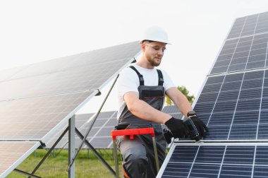 Güvenlik teçhizatı takan erkek işçi yenilenebilir enerji çiftliğine güneş panelleri yerleştiriyor, temiz enerji üretimini birbirine bağlıyor.