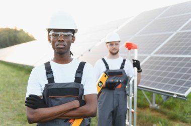 Güneş panelleri kuran mühendisler ve işçiler sürdürülebilir enerjiye katkıda bulunuyor ve yeşil bir alanda takım çalışması gösteriyor