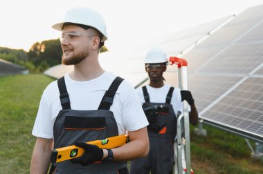 Çeşitli işçiler bir enerji santraline güneş panelleri kuruyor, temiz elektrik üretimini ve sürdürülebilir kalkınmayı destekliyor