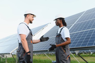 Çeşitli mühendisler, yenilenebilir enerji çözümleri ve sürdürülebilir enerji üretimini tartışarak, güneş paneli kurulumunda işbirliği yapıyorlar.