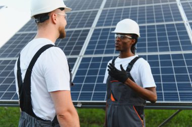 İki farklı teknisyen, büyük bir güneş paneli önünde iş konuşuyorlar.