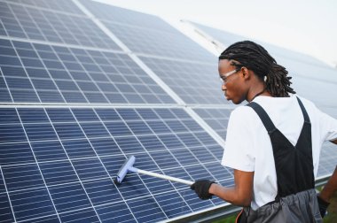 Teknisyen cam sileceği ile güneş paneli yüzeyini temizliyor, elektrik üretimi için optimal verimliliği sağlıyor