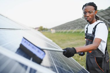 Genç adam güneş panellerinde bakım yapıyor, ideal yenilenebilir enerji üretimi için temiz yüzeyler sağlıyor