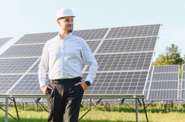 Güneş panellerinin önünde duran sert şapka takan mühendis, enerji santralindeki yenilenebilir enerji üretimini denetliyor.