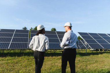 Güneş panellerini denetleyen, güneş çiftliğinde yenilenebilir enerji çözümleri planlayan sert başlıklar takan mühendisler