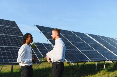 Çeşitli mühendisler güneş panelleri arasında dizüstü bilgisayarla sohbet ederek sürdürülebilir enerji çözümleri planlıyorlar.