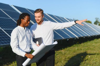 İki farklı mühendis planlarını tartışıyor ve bir güneş enerjisi çiftliğinde yenilenebilir enerji projesi planlıyor.