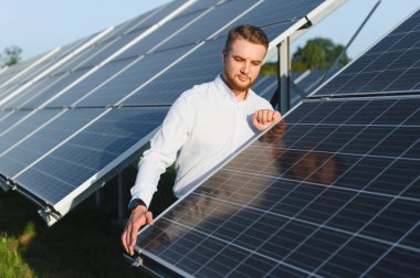 Bir güneş çiftliğindeki fotovoltaik panelleri inceleyen erkek mühendis, yenilenebilir enerji üretimi için sürdürülebilir uygulamalar uyguluyor