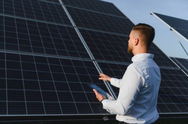 Güneş çiftliğindeki fotovoltaik panelleri gözlemleyen mühendis, yeşil enerji teknolojisinin veri analizi ve bakımı için bir tablet tutuyor.