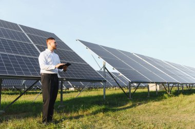 Güneş paneli alanını inceleyen erkek mühendis veri analizi için dijital tablet kullanıyor. Yenilenebilir enerji üretimi kavramı