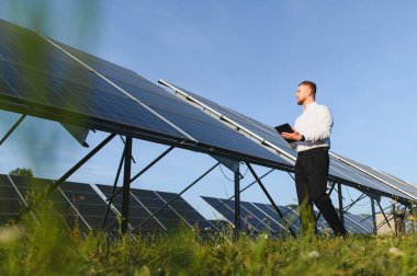 Dijital tablet tutan, güneş panelleri arasında yürüyen, verimli yenilenebilir enerji üretimi sağlayan adam