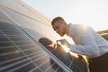 Fotovoltaik panelleri inceleyen genç adam, sürdürülebilir temiz enerji üretimi için optimal performans sağlıyor. Güneş parıldıyor mercek patlaması yaratıyor