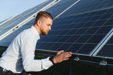 Genç adam, sürdürülebilir enerji ve yeşil teknolojiyi temsil eden bir fotovoltaik enerji istasyonunda güneş panelini inceliyor.
