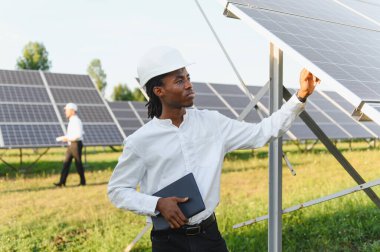 Sert şapka mühendisi güneş paneli dizisini büyük güneş çiftliğinde tabletle denetliyor, yenilenebilir enerji üretimi ve bakımını izliyor