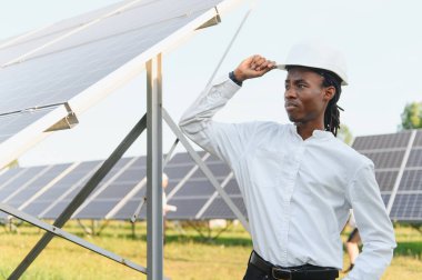 Siyah şapkalı genç adam güneş panellerini denetliyor, sürdürülebilir teknoloji ve temiz enerji gelişimini temsil ediyor.
