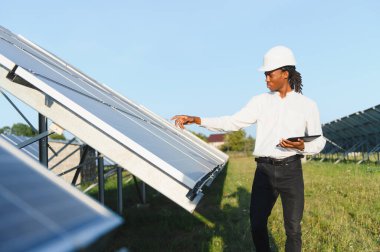 Bir enerji santralinde sürdürülebilir enerji üretimini sağlamak için güneş panellerini tabletle kontrol eden bir mühendis.