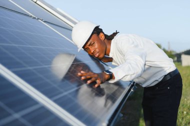 Sert şapka içindeki Afrikalı Amerikalı mühendis yenilenebilir enerji alanındaki güneş pili yüzeyini kontrol ederek verimlilik ve sürdürülebilirliği sağlıyor.