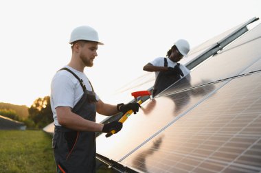 Sert şapkalar takan iki teknisyen büyük bir güneş çiftliğine temiz yenilenebilir enerji üreten güneş panelleri kuruyor.