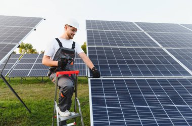 Sert şapka ve eldiven giyen işçiler kırsal bir güneş çiftliğine fotovoltaik güneş panelleri kuruyor, yenilenebilir, temiz enerji çözümleri geliştiriyor