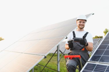 Güneş enerjisi santralinde çalışan bir güneş teknisyeni elinde matkap ve onay veriyor.