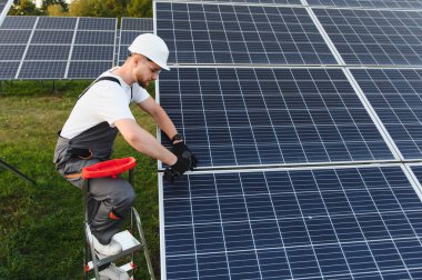 Sert şapkalı bir adam bir enerji santraline güneş panelleri kuruyor, yenilenebilir enerji sürdürülebilirliğine odaklanıyor