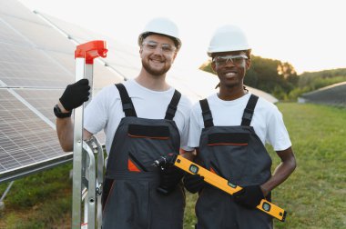 Güneşli bir alana güneş panelleri kuran çeşitli mühendisler, sürdürülebilir temiz enerji üretimi için araçlar ve takım çalışması kullanıyorlar