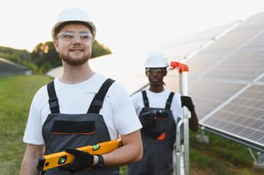 Koruyucu ekipmanlı bir grup teknisyen yeşil enerji çiftliğine güneş panelleri kuruyor, temiz enerjiyi destekliyorlar.