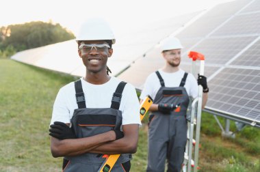 Çeşitli mühendisler, yeşil enerjiyi, takım çalışmasını ve yenilenebilir elektrik üretimini sembolize ederek bir güneş enerjisi santraline gülümsüyor.