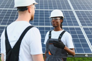 İki farklı teknisyen açık havada güneş paneli alanında yenilenebilir enerji projesini tartışıyor. Temiz enerjiyi teşvik etmek