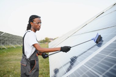 Bir enerji santralinde güneş panellerini temizleyen Afrikalı Amerikalı teknisyen verimli bir yenilenebilir enerji üretimi ve sürdürülebilir bir gelecek sağlıyor.