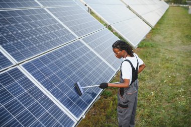 Güneş panellerini temizleyen, güneş enerjisi çiftliğinde bakım yapan Afrikalı Amerikalı işçiler. Sürdürülebilir teknolojiyi teşvik etmek