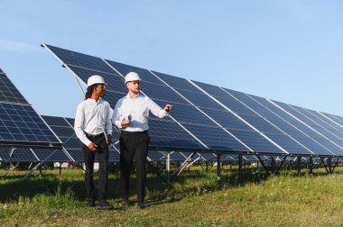 Güneş enerjisi santralinde yürüyen ve planlarını tartışan iki mühendis yenilenebilir enerji ve sürdürülebilirliğe odaklanıyor.