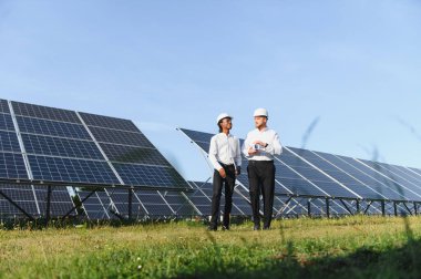 Çeşitli mühendisler sürdürülebilir elektrik için yenilenebilir enerji teknolojisini yöneten bir güneş enerjisi santralinde çalışmayı tartışıyor.