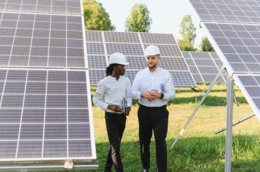 Dayanıklı kasklar takan mühendisler güneş enerjisi istasyonunda yürürken sürdürülebilir teknoloji çözümlerini tartışıyorlar.