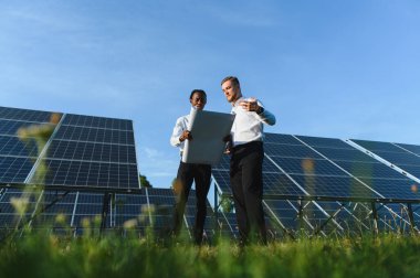 Bir güneş enerjisi santralinin planlarını inceleyen çeşitli mühendisler, takım çalışmasına ve sürdürülebilir enerji geliştirmesine odaklanıyorlar.