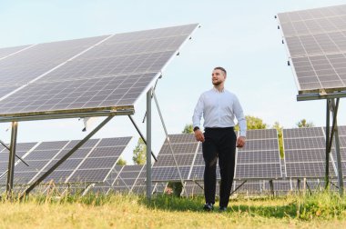 Modern bir güneş paneli alanında yürüyen iş adamı, yeşil enerji, sürdürülebilir teknoloji ve çevresel sorumluluk sergiliyor